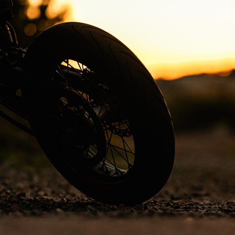 Motorcycle silhouette on gravel road at dusk.